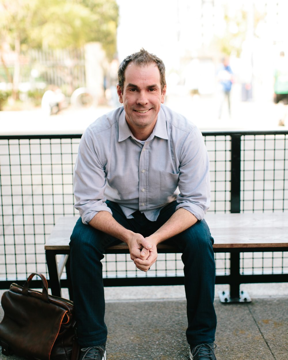 Rick Mulready sitting on a bench outside, smiling